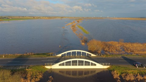 Oversvømmede områder i et fladt landskab og en bro, der næsten står under vand. Foto: Jammerbugt Kommune